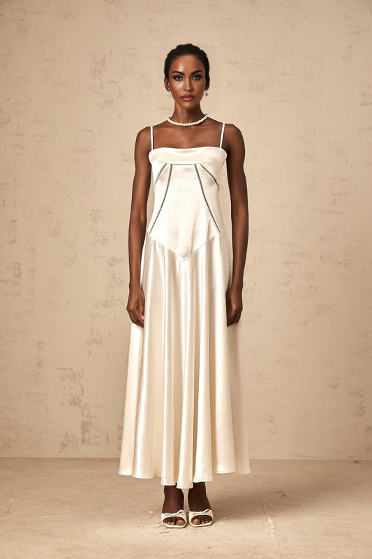 A woman wearing a long white satin dress with a flared skirt standing against a plain background