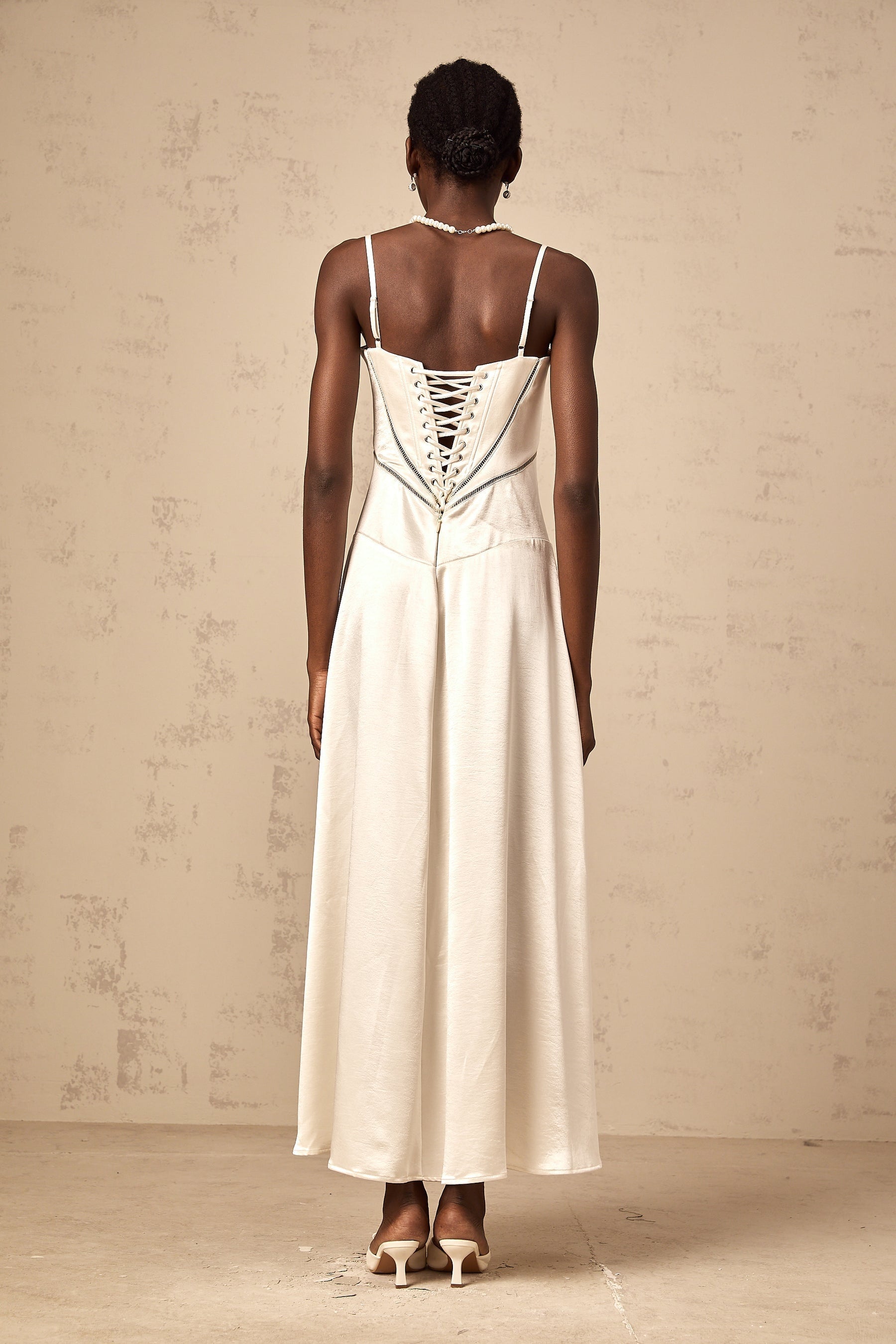A woman wearing a long white satin maxi dress with a flared skirt and fitted bodice standing in a relaxed pose