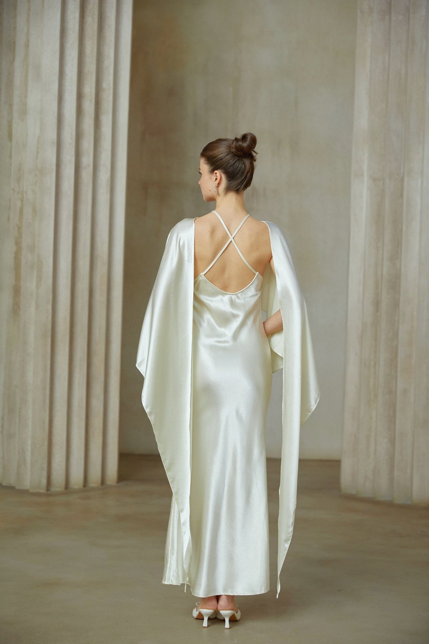 A woman wearing a long white satin maxi dress with shawllike panels draping from the shoulders flowing to the floor elegant and graceful design suitable for formal occasions
