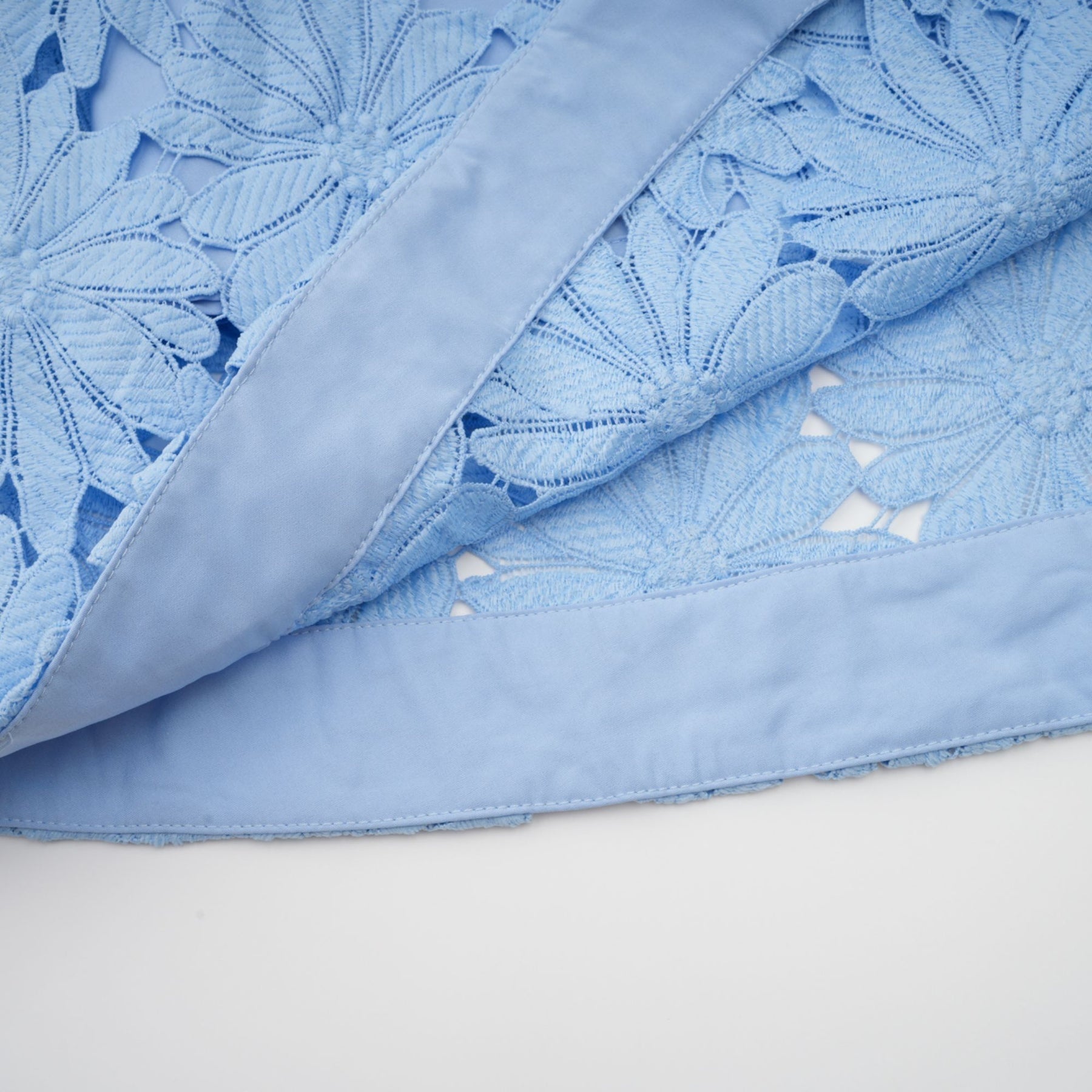 A woman wearing a matching blue lace top and skirt set with intricate floral patterns standing against a plain background