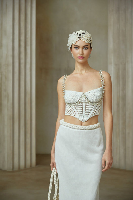 A woman wearing a matching crochet knit two piece outfit consisting of a sleeveless crop top and a midi skirt in a light color