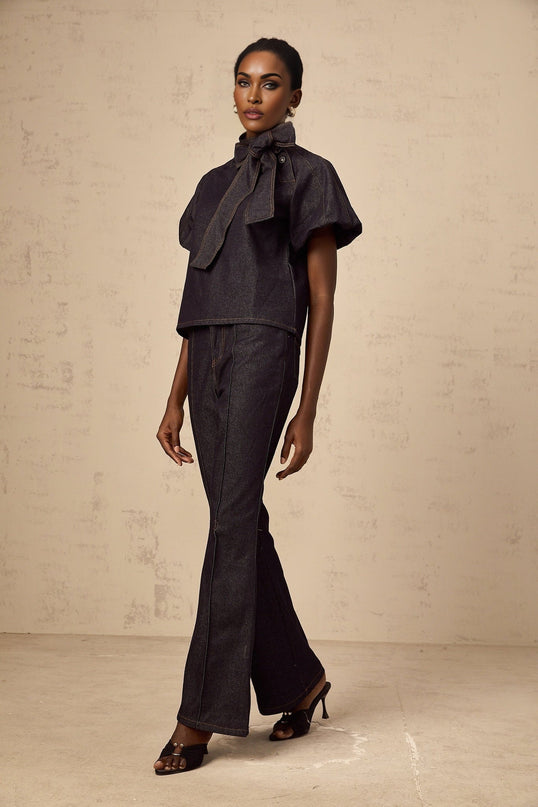 A woman wearing a matching denim outfit consisting of an indigo blue blouse and jeans with contrasting light stitching visible on both pieces