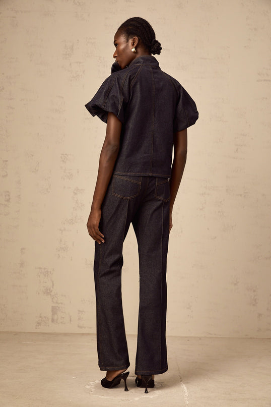 A woman wearing a matching denim outfit with an indigo blue blouse and jeans featuring contrast stitching The set is called Roxane