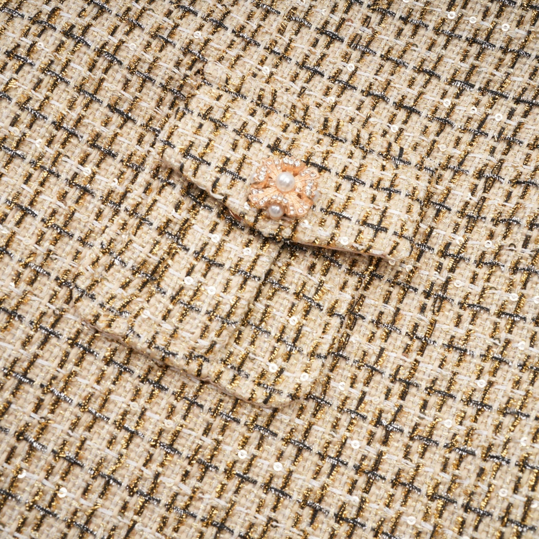 A woman wearing a matching gold tweed jacket and skirt set with sequin embellishments The jacket has long sleeves and the skirt is knee length Both pieces shimmer in the light