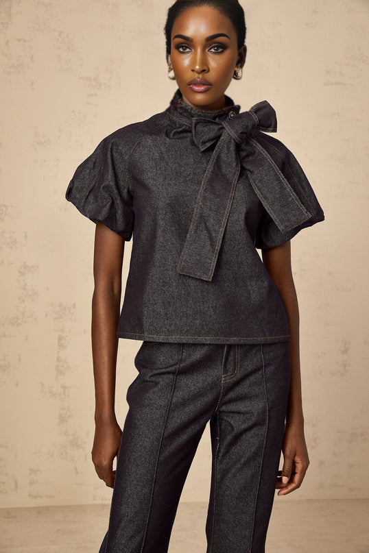 A woman wearing a matching indigo blue denim outfit consisting of a buttoned blouse and jeans with contrasting white stitching visible throughout both pieces