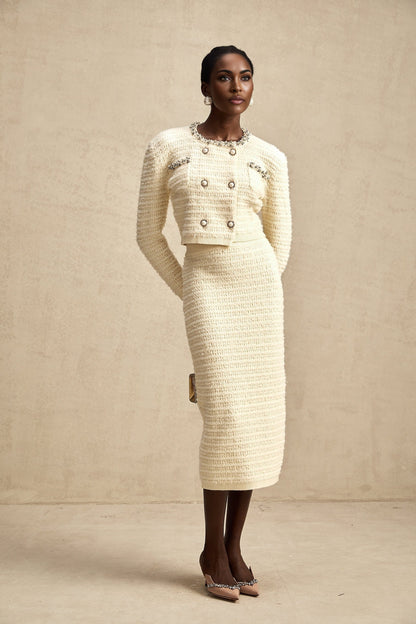 A woman wearing a matching knit cardigan and skirt set with embellishments The cardigan is open in the front and the skirt falls to about knee length The set is likely in a light color with decorative details
