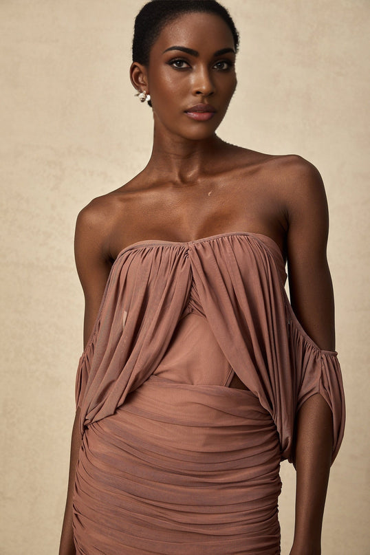 A woman wearing a matching offshoulder bodysuit and skirt set in a light color standing against a plain background