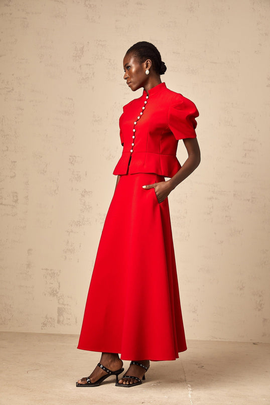 A woman wearing a matching red outfit consisting of a pleated blouse and skirt The blouse has a loose fit with long sleeves while the skirt falls to about knee length Both pieces feature pleated details giving the set a stylish and coordinated appearance