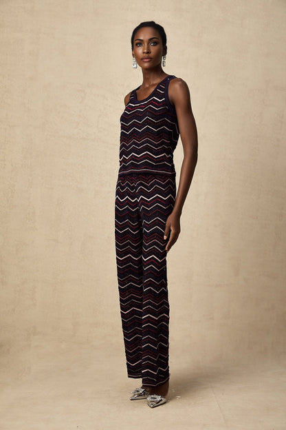 A woman wearing a matching set consisting of a crochet knit top and trousers with a zigzag pattern in a light color The top has short sleeves and the trousers are wide legged