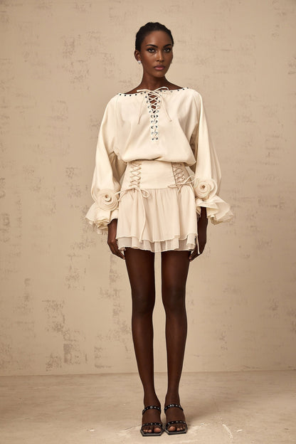 A woman wearing a matching set consisting of a light colored ruffled blouse with self tie details and a coordinating skirt