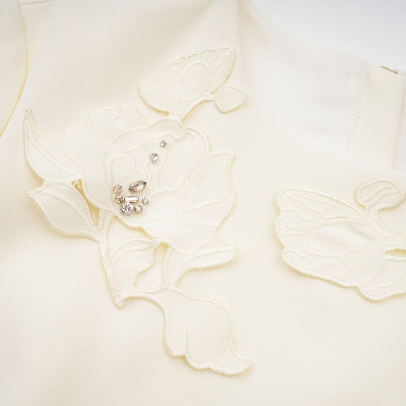 A woman wearing a matching set consisting of a sleeveless crop top and high waisted skirt in neutral colors The set features a textured 3D petal design covering both pieces