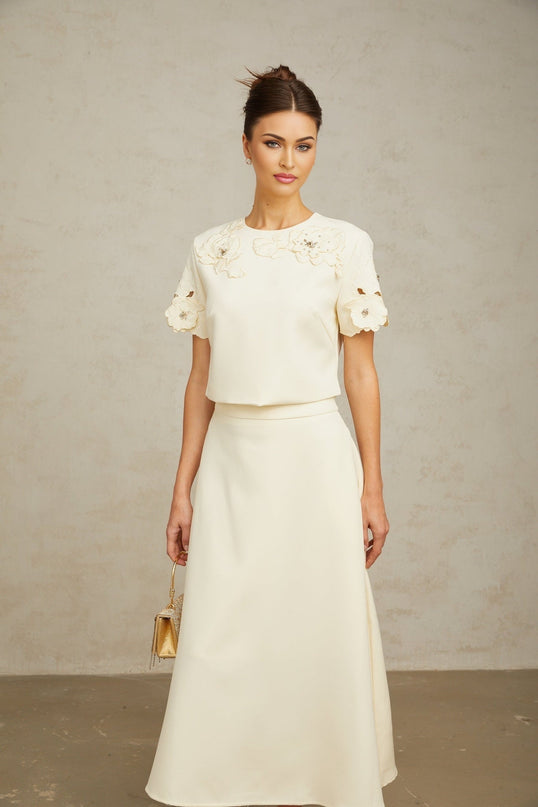 A woman wearing a matching set consisting of a sleeveless top and skirt in neutral tones The outfit features delicate threedimensional petal details for texture and visual interest