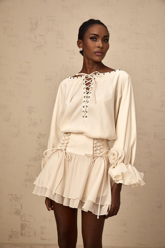 A woman wearing a matching set consisting of a white ruffled blouse with selftie details and a coordinating skirt standing against a plain background