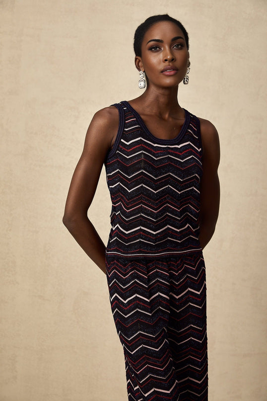 A woman wearing a matching set of a zigzag patterned crochet knit top and trousers in a neutral color The top has short sleeves and the trousers are wide legged The set has a bohemian summer style