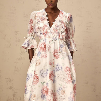 A woman wearing a midi dress with a vibrant three dimensional floral print featuring petal designs in various colors against a light background