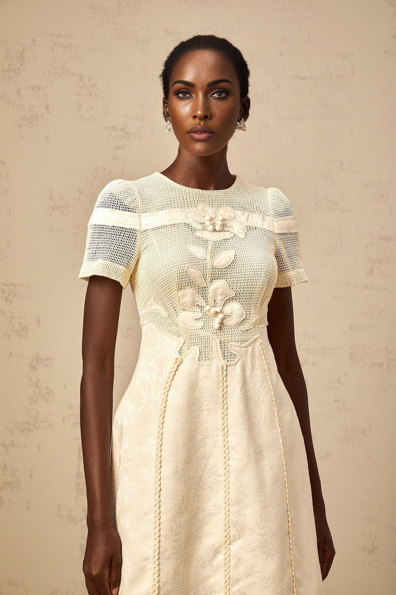 A woman wearing a midi length dress with floral embroidery and openwork details