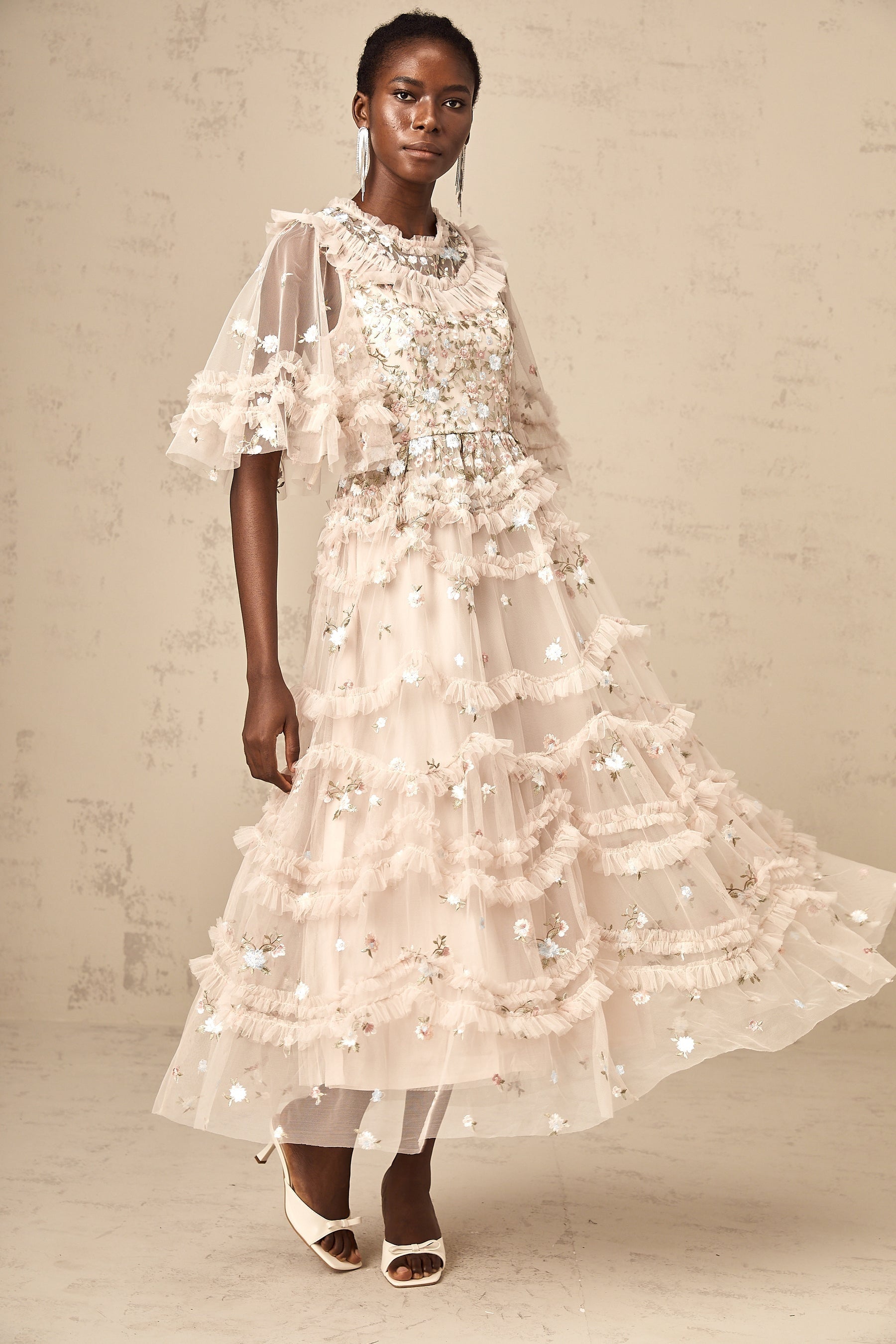 A woman wearing a midi length dress with tiered ruffles and floral embroidery design standing in a relaxed pose