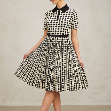 A woman wearing a midi length knit dress with color blocked sections and polka dot patterns in contrasting colors