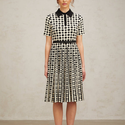 A woman wearing a midi length knit dress with color blocked sections and polka dot patterns in contrasting colors