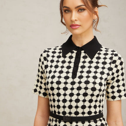 A woman wearing a midi length knit dress with color blocked sections and polka dot patterns in contrasting colors