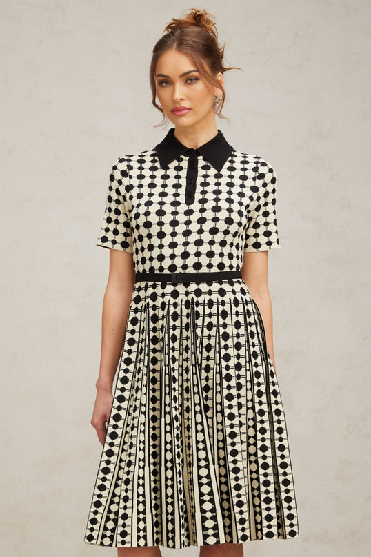 A woman wearing a midi length knit dress with color blocked sections and polka dot patterns in contrasting colors