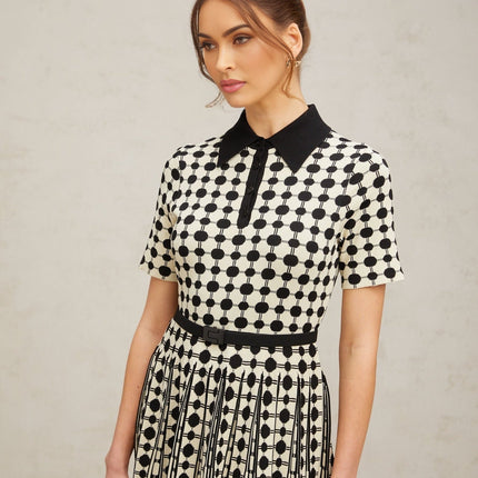 A woman wearing a midi length knit dress with color blocked sections and polka dot patterns in contrasting colors