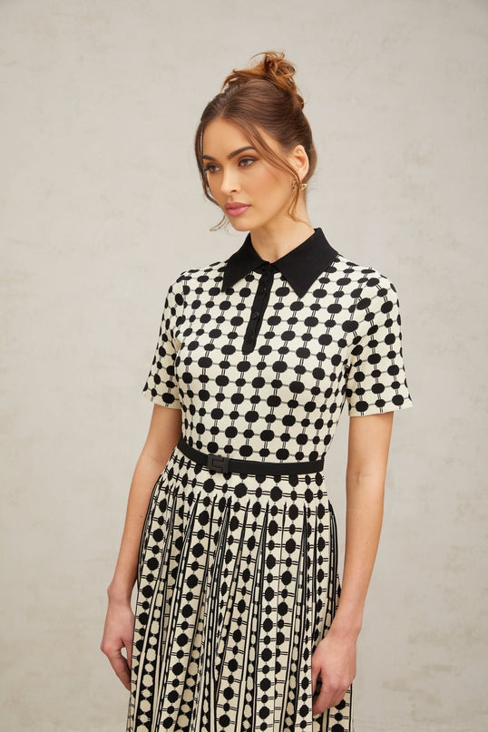 A woman wearing a midi length knit dress with color blocked sections and polka dot patterns in contrasting colors