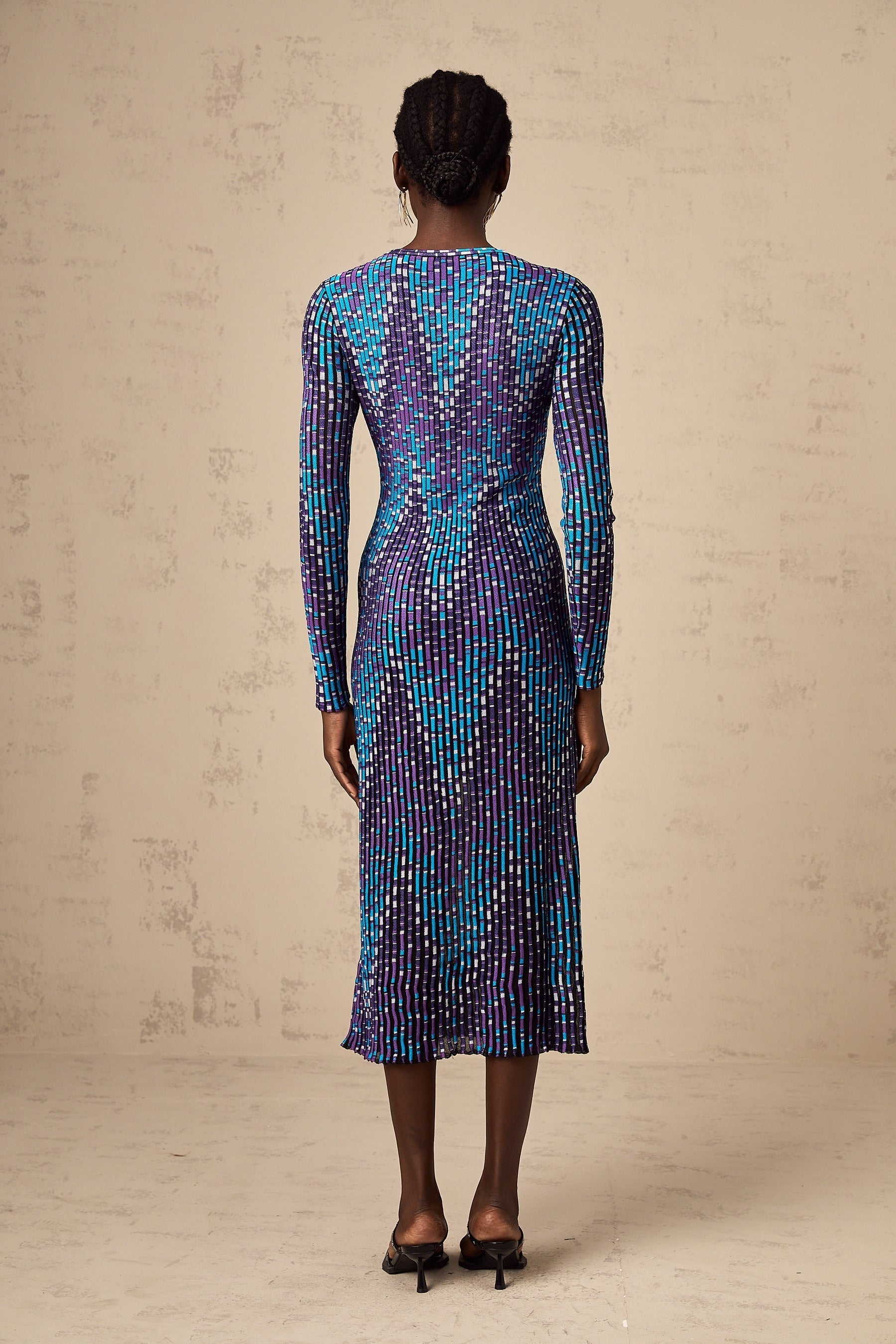 A woman wearing a midi length knitted dress with a zigzag pattern standing in a relaxed pose