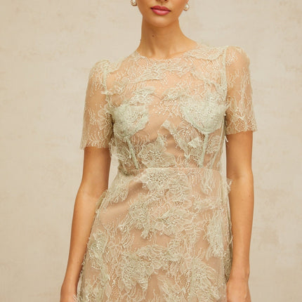 A woman wearing a mintgreen midi dress made of floral lace standing in a neutral background
