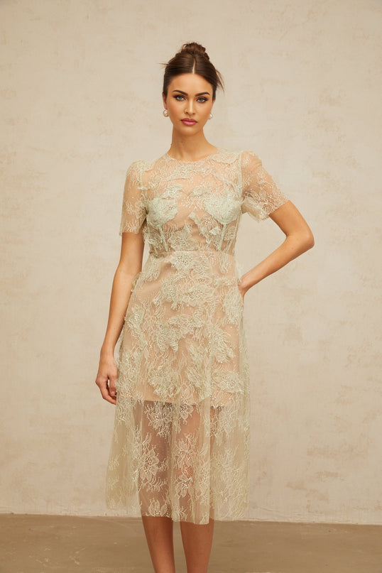 A woman wearing a mintgreen midi dress with floral lace pattern standing against a plain background