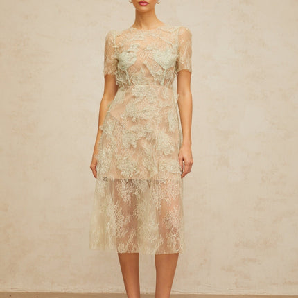 A woman wearing a mintgreen midi dress with floral lace pattern standing against a plain background