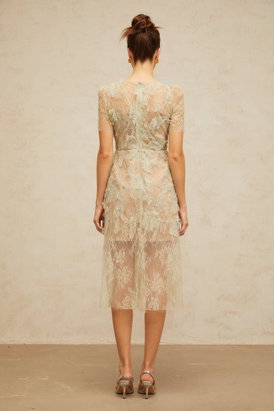 A woman wearing a mintgreen midi dress with floral lace pattern standing in a relaxed pose