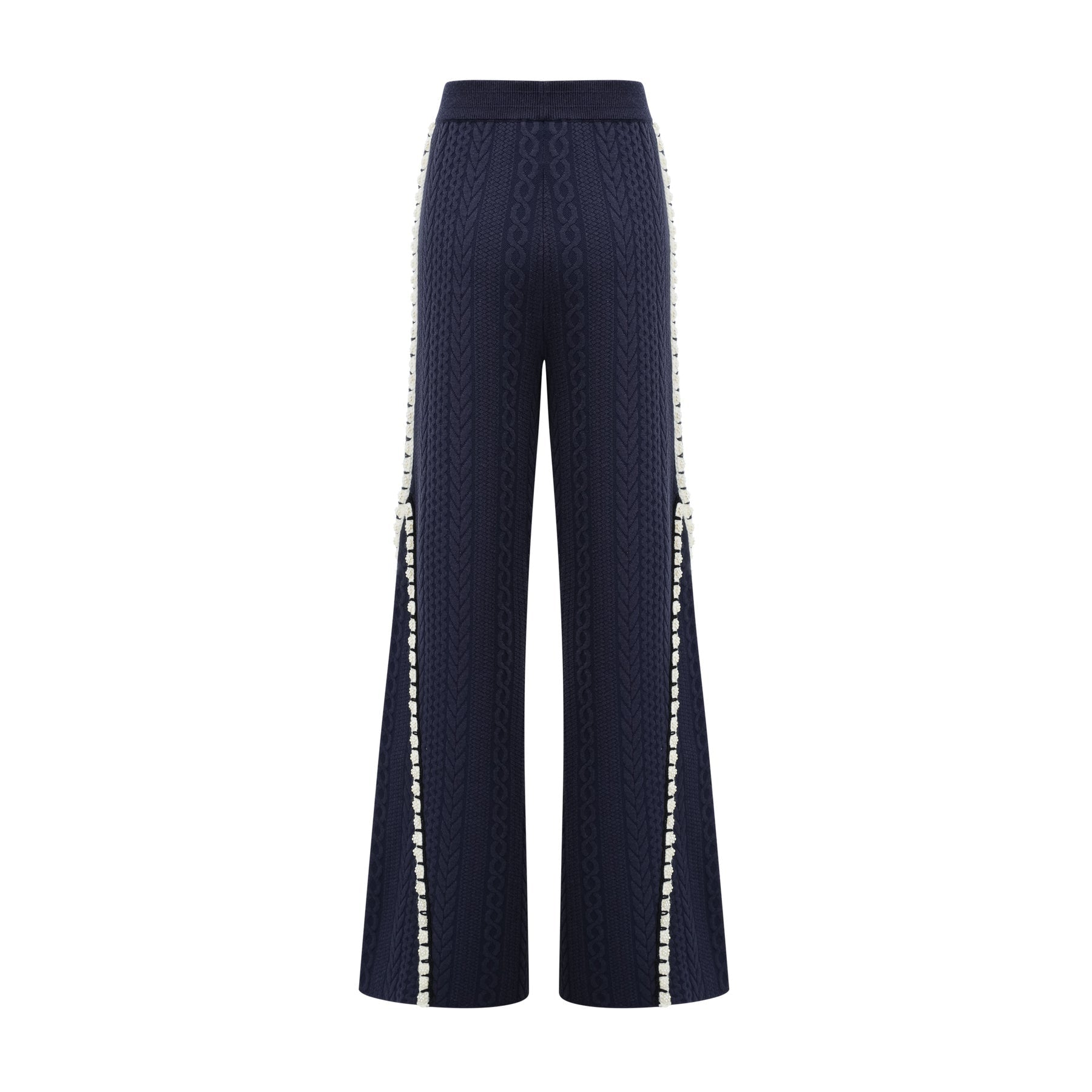 A woman wearing a navy blue crochet knit cardigan and matching trousers standing against a plain background