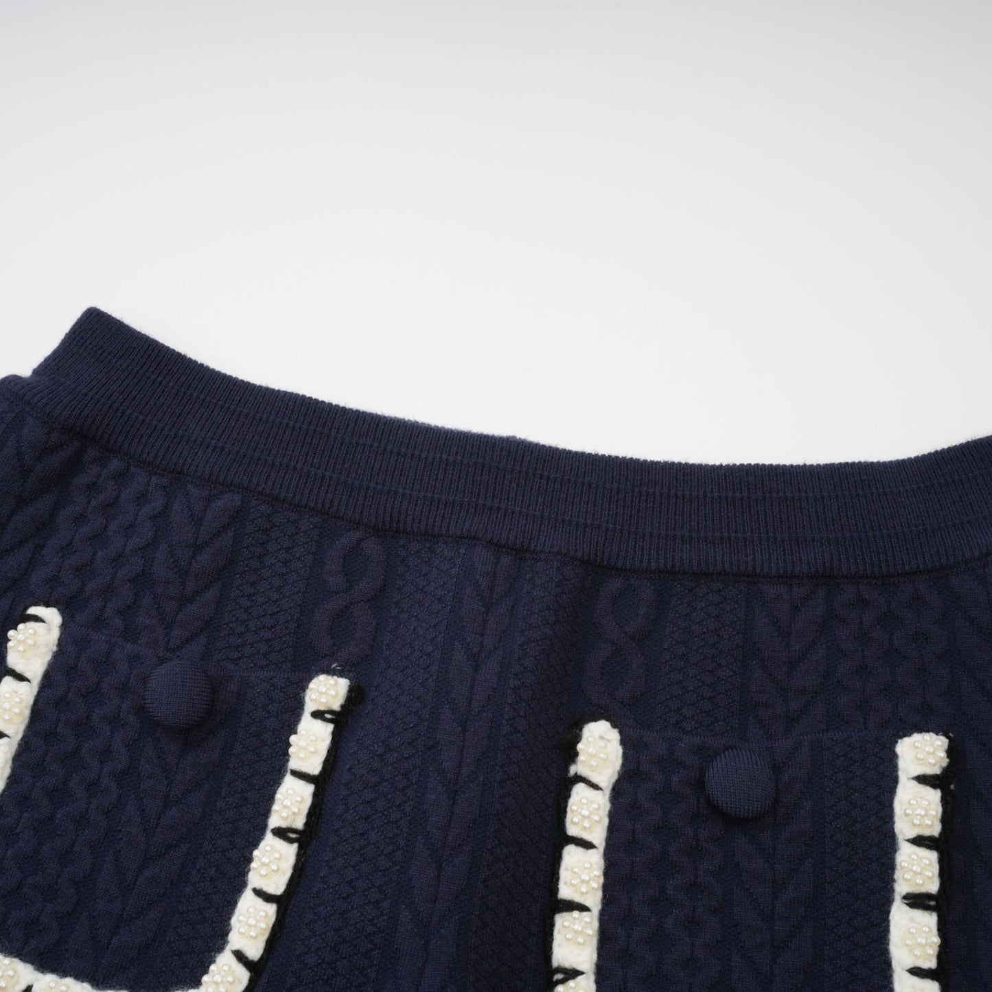 A woman wearing a navy blue crochet knit cardigan and matching trousers standing against a plain background