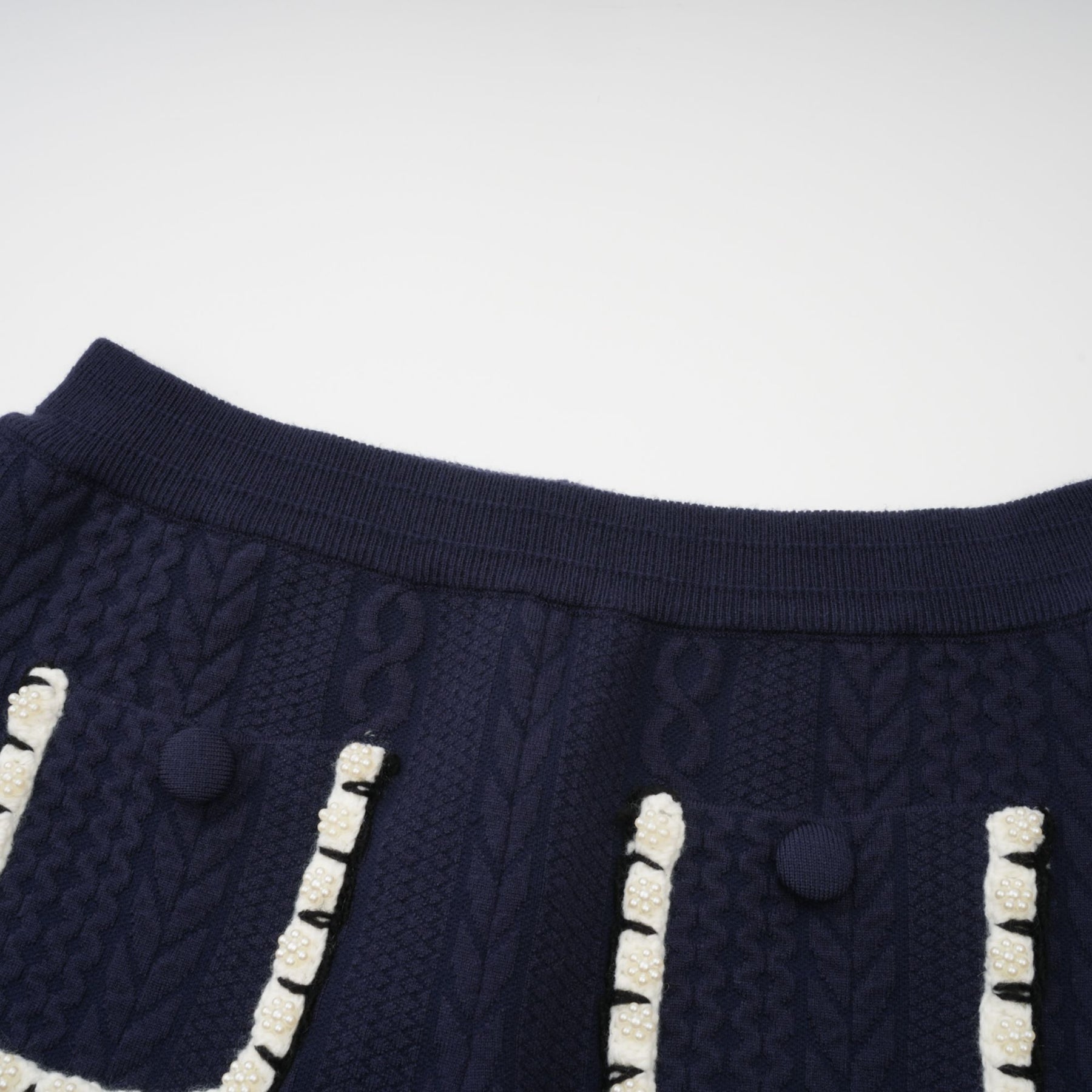 A woman wearing a navy blue crochet knit cardigan and matching trousers standing against a plain background