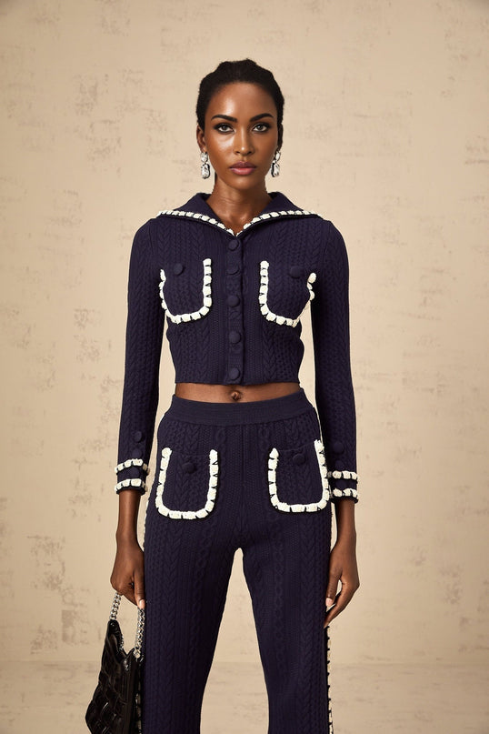 A woman wearing a navy blue crochet knit cardigan and matching trousers standing against a plain background