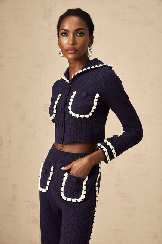 A woman wearing a navy blue crochet knit cardigan and matching trousers standing against a plain background