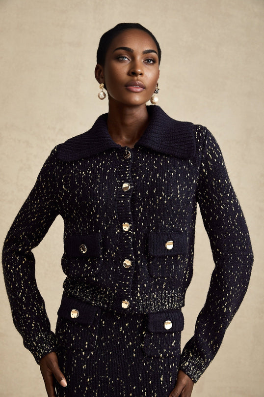 A woman wearing a navy blue crochet knit jacket and matching skirt set standing against a plain background