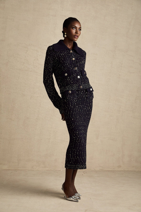 A woman wearing a navy blue crochet knit jacket and matching skirt set standing against a plain background