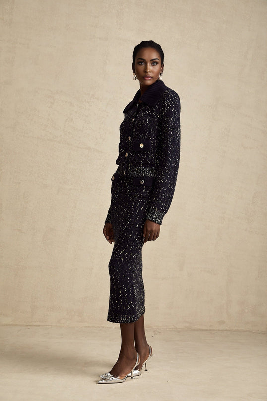 A woman wearing a navy blue crochet knit jacket and matching skirt set standing against a plain background