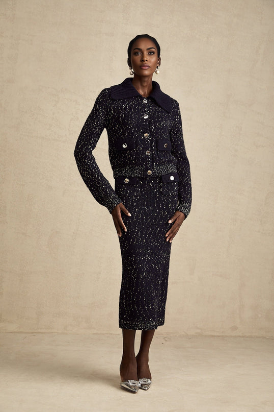 A woman wearing a navy blue crochet knit jacket paired with a matching skirt standing against a plain background