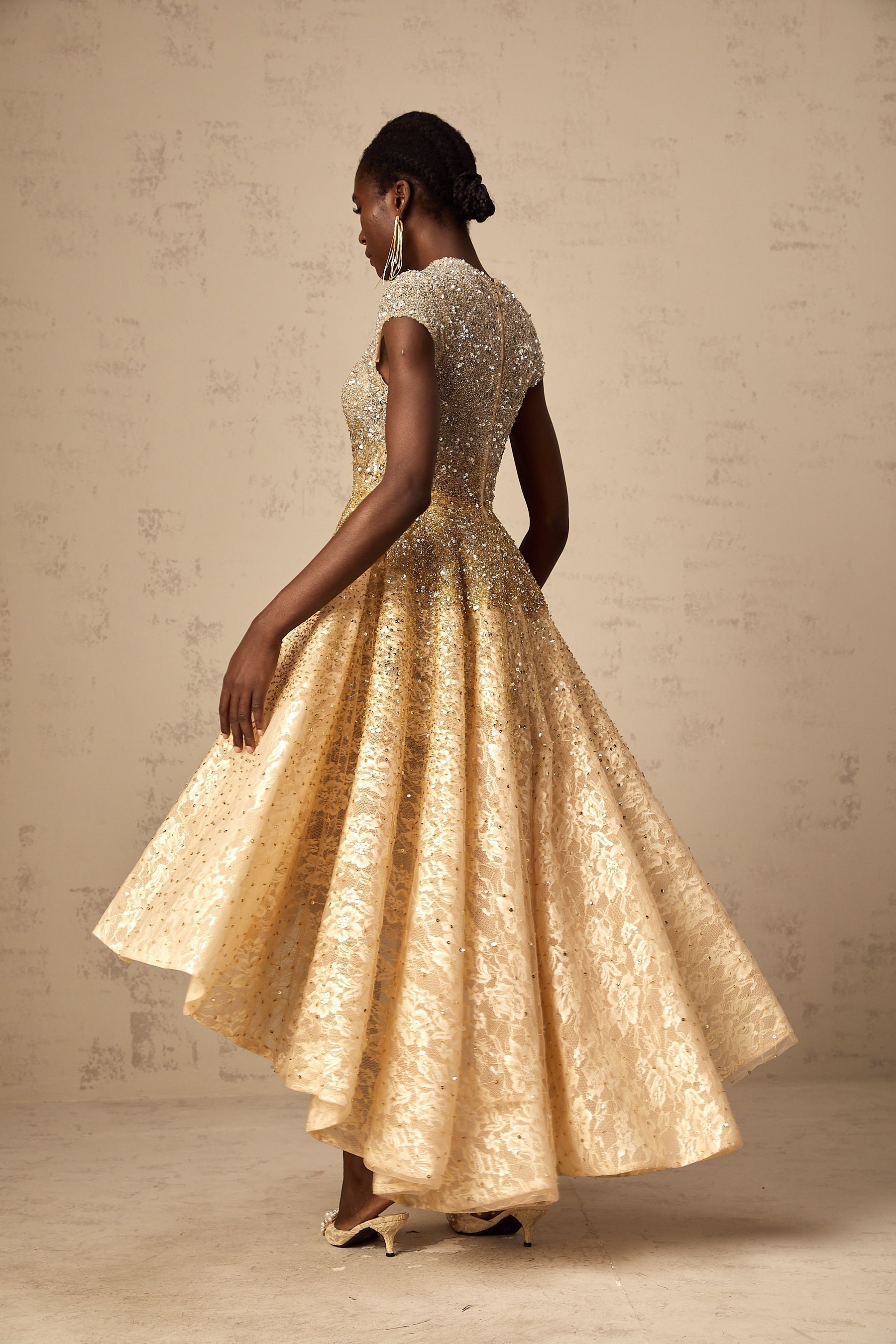 A woman wearing a neutral colored sequined dress with a high low hemline