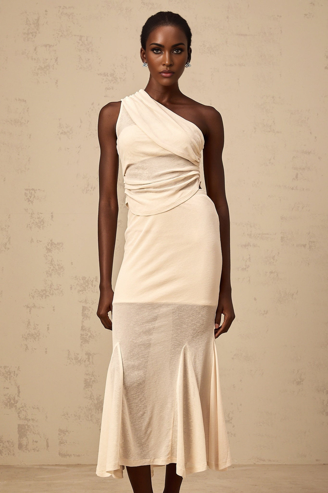 A woman wearing a neutralcolored matching set consisting of a ruched stretch top and skirt named Gwenaelle The outfit has a formfitting design with gathered fabric details