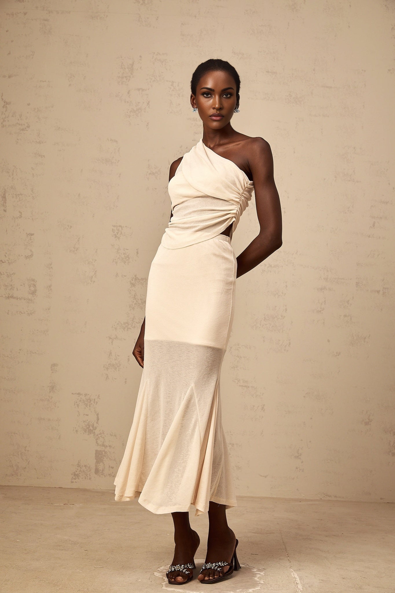 A woman wearing a neutralcolored matching set consisting of a ruched stretch top and skirt The outfit has a formfitting design with gathered fabric details