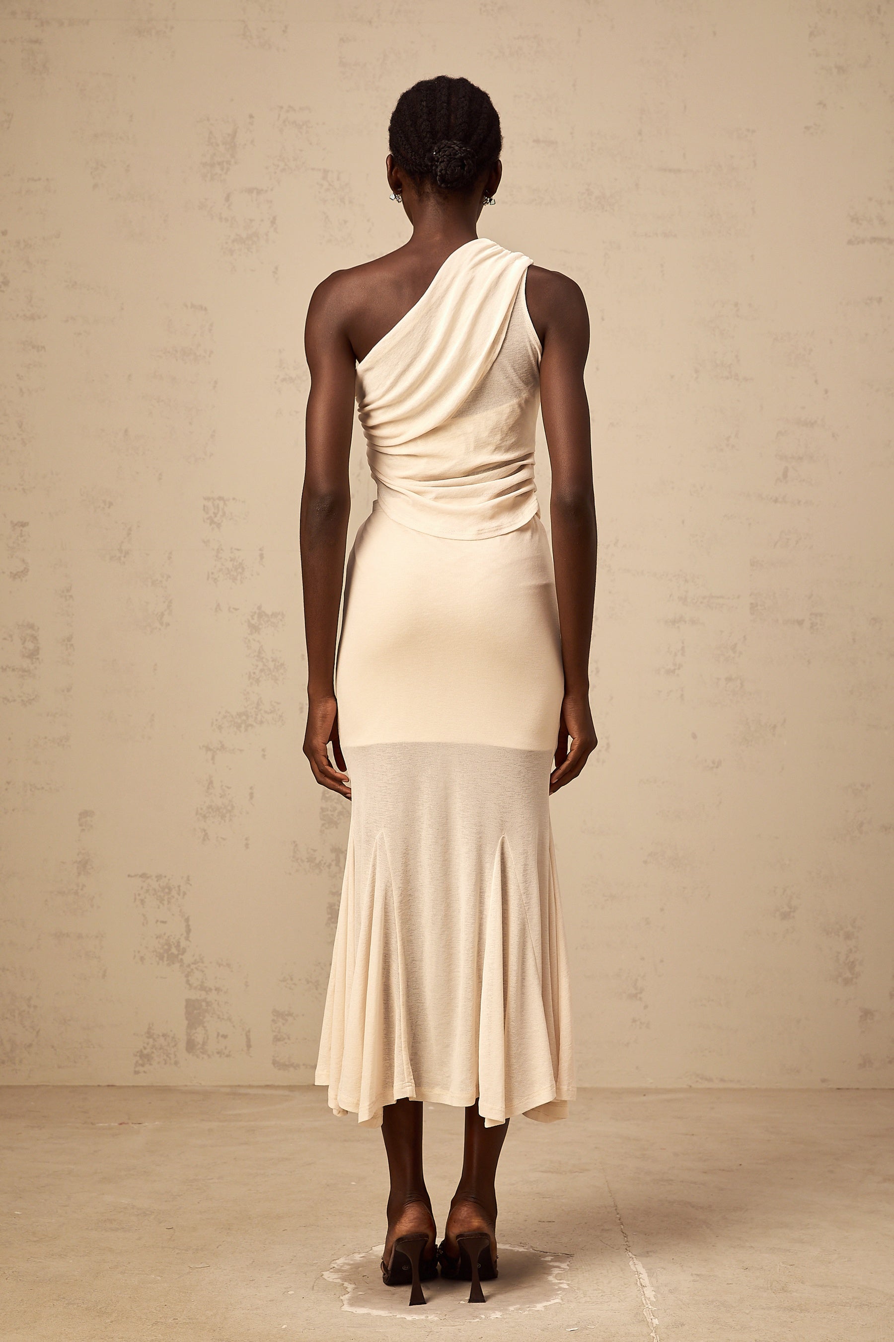 A woman wearing a neutralcolored matching set consisting of a stretch ruched top and skirt The top features long sleeves and the skirt has a formfitting silhouette Both pieces have a textured ruched design throughout