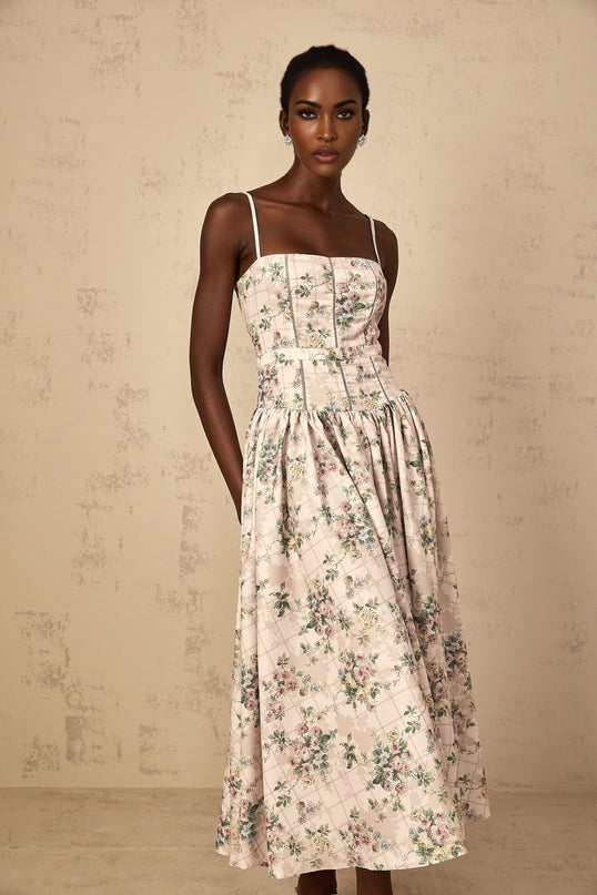 A woman wearing a neutralcolored midi dress with a delicate floral print pattern standing in a relaxed pose