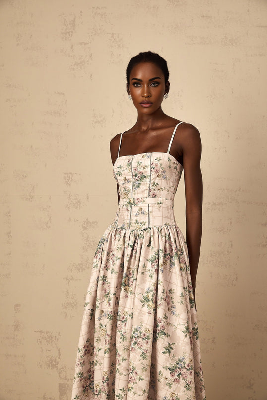 A woman wearing a neutralcolored midi dress with a delicate floral print standing in a relaxed pose