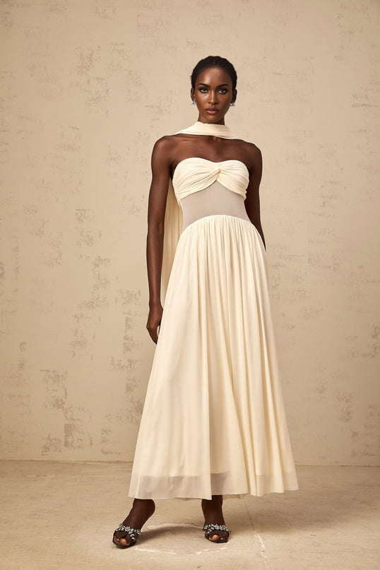 A woman wearing a neutralcolored midi dress with a scarfinspired mesh design and delicate pattern detailing