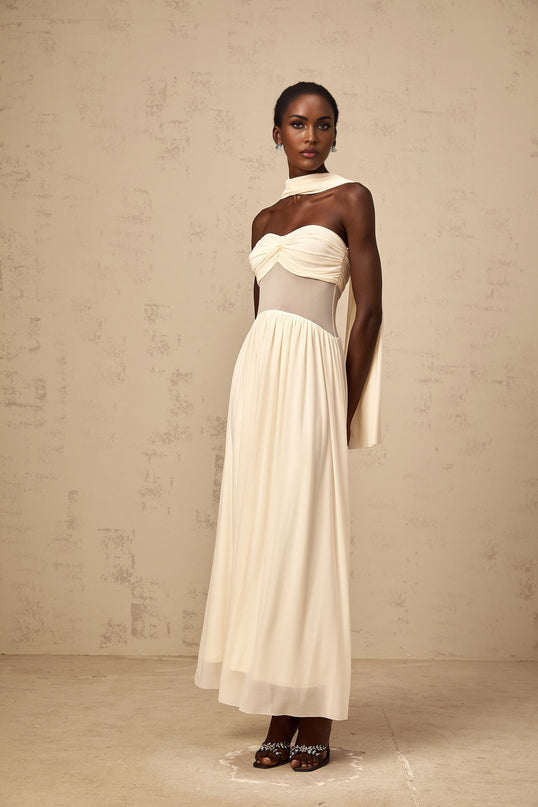 A woman wearing a neutralcolored midi dress with a scarfinspired mesh design and flowy silhouette