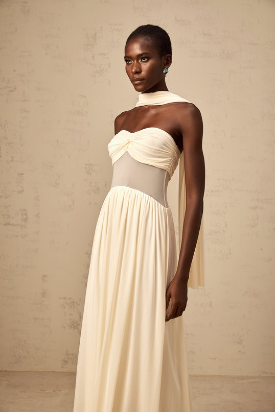 A woman wearing a neutralcolored midi dress with a scarfinspired mesh design featuring flowy fabric and delicate patterns